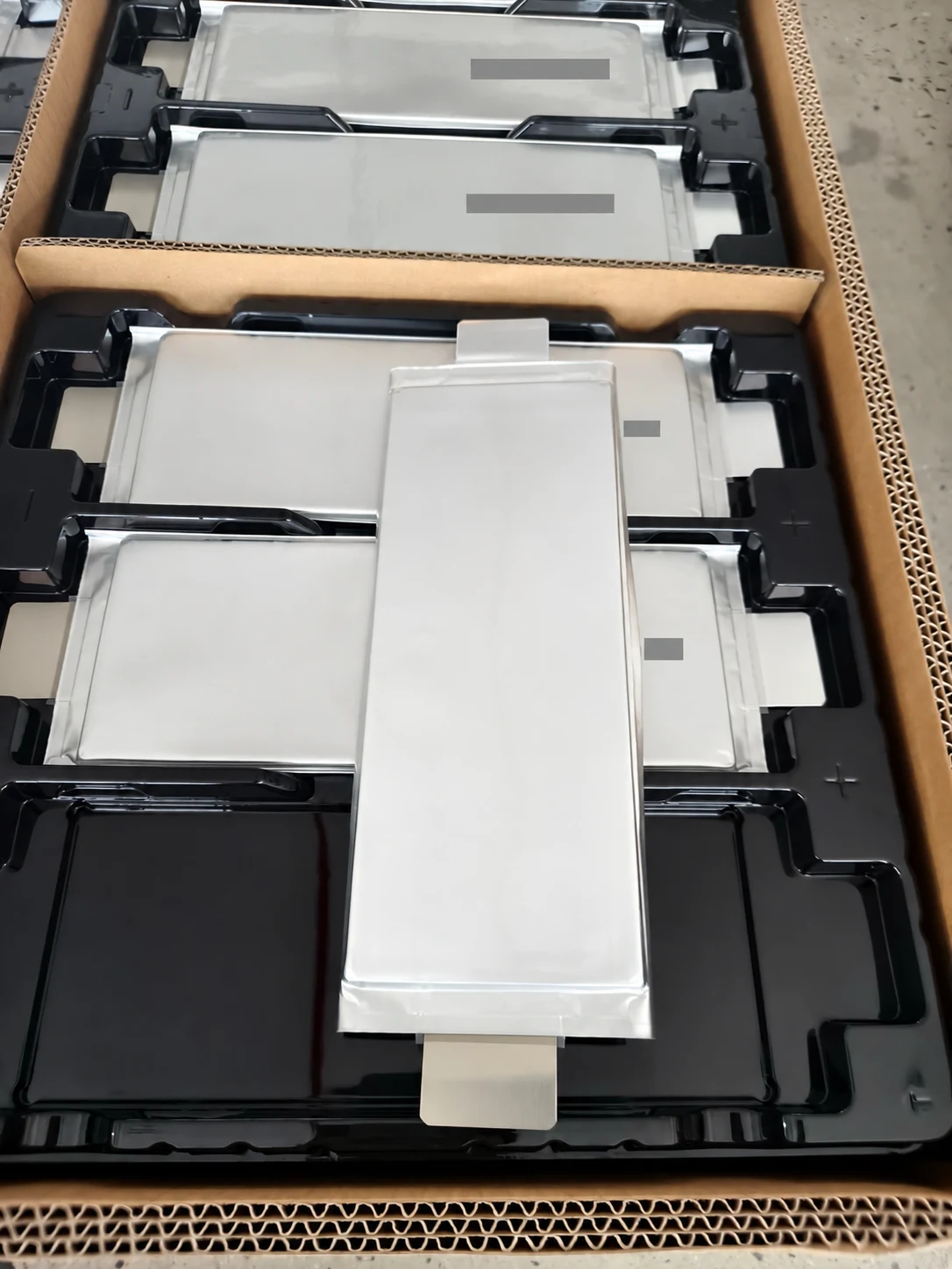 Customer-supplied photograph of pouch cells in packaging; tracking marks masked.